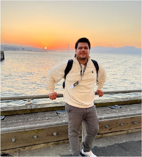 Andres Carreon smiling on a pier at sunset, with a bridge across the bay behind him